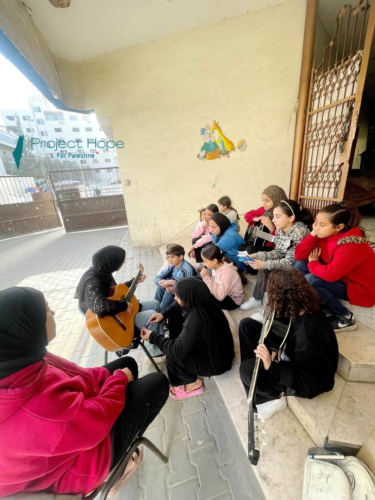 Children gathered around a guitarist during a Project Hope music session in Gaza