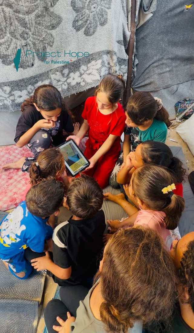 Children share a tablet inside an orphan camp we support.